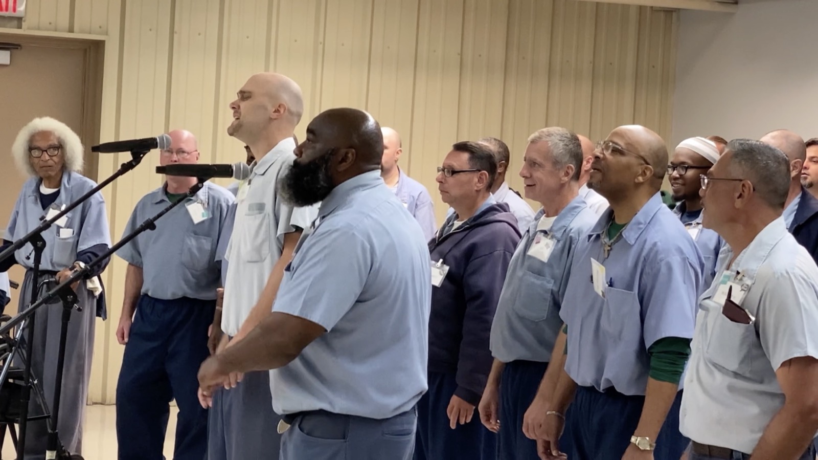 A long row of choir members singing, with a soloist stepping toward the microphone at the left.