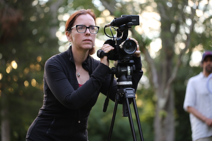 Director Gabrielle C. Burton behind a camera on a tripod, filming outdoors.
