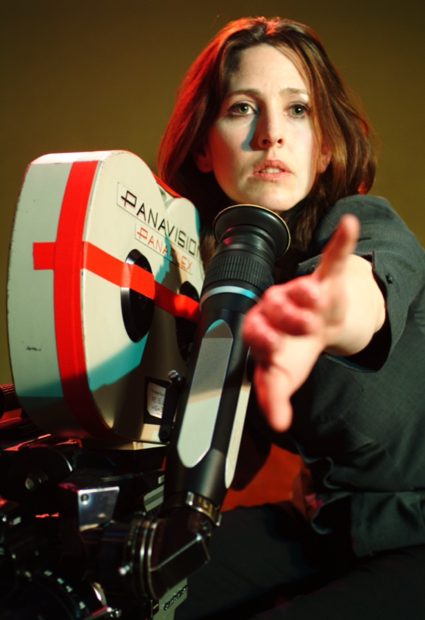 Director Ursula Burton beside a 35mm Panavision camera, pointing to direct a shot.